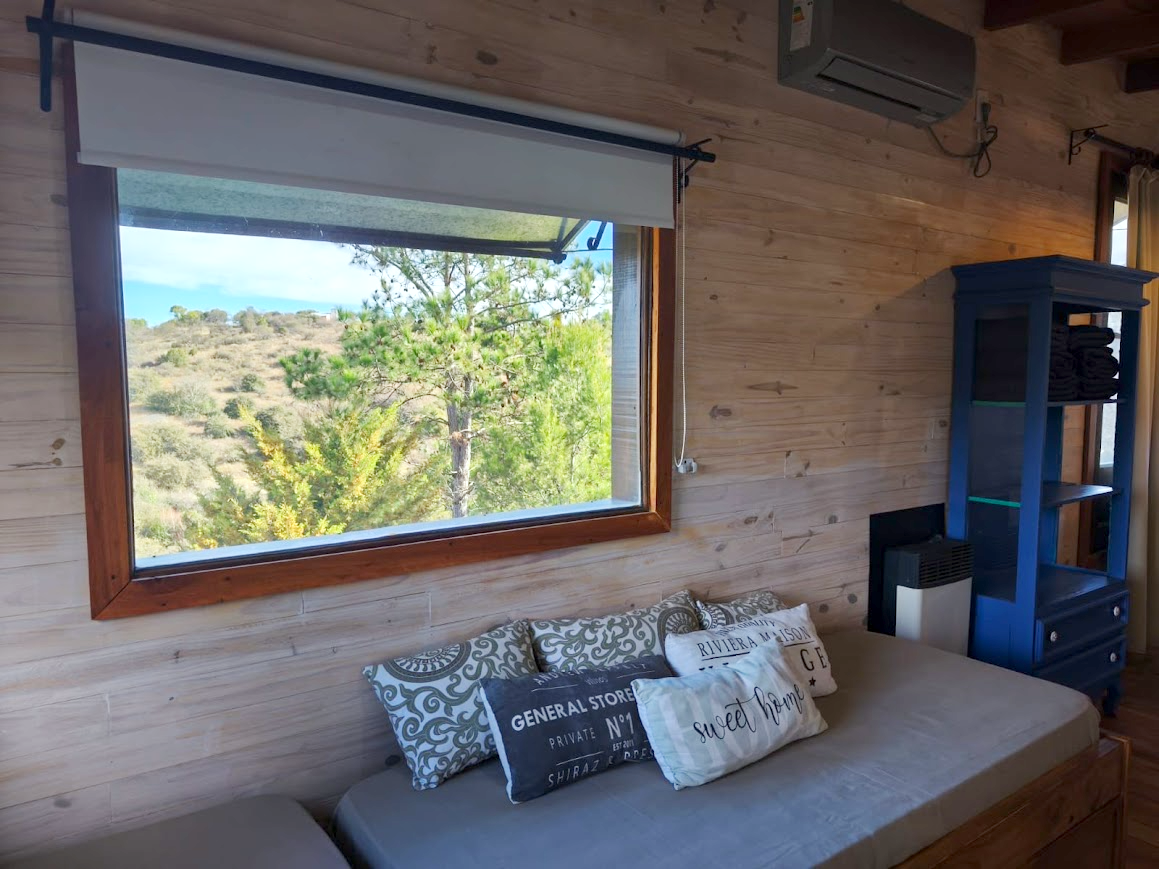 Living de la Cabaña Chuña 2 con aire acondicionado y ventanal a las sierras